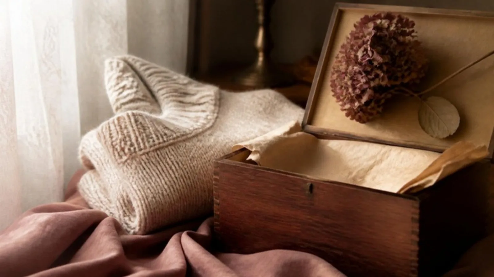 Un pull en maille plié et une boîte en bois ouverte avec une hortensia séchée près de la fenetre